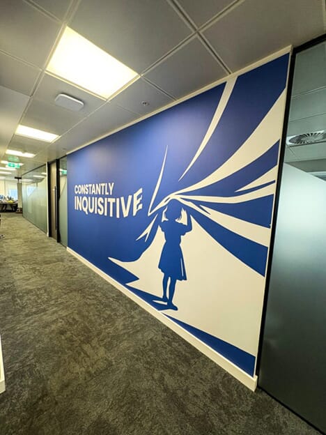 An image of the dark blue "Constantly Inquisitive" wall graphic showing a child lifting up a curtain.